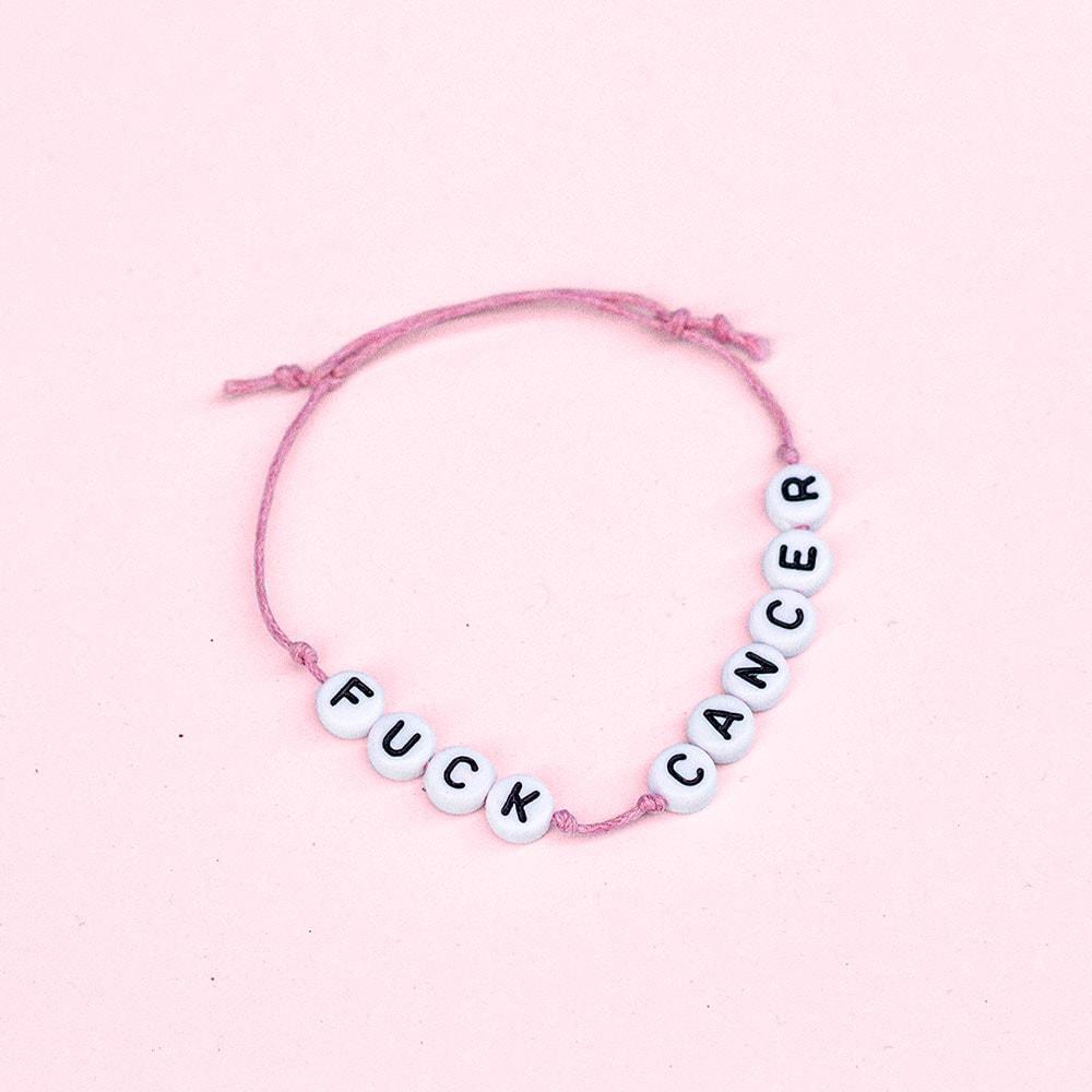 Rosa trådarmband som det står "FUCK CANCER" på